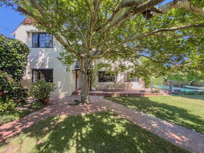Rear view of the property featuring a brick paved patio, mature garden, and a swimming pool area.