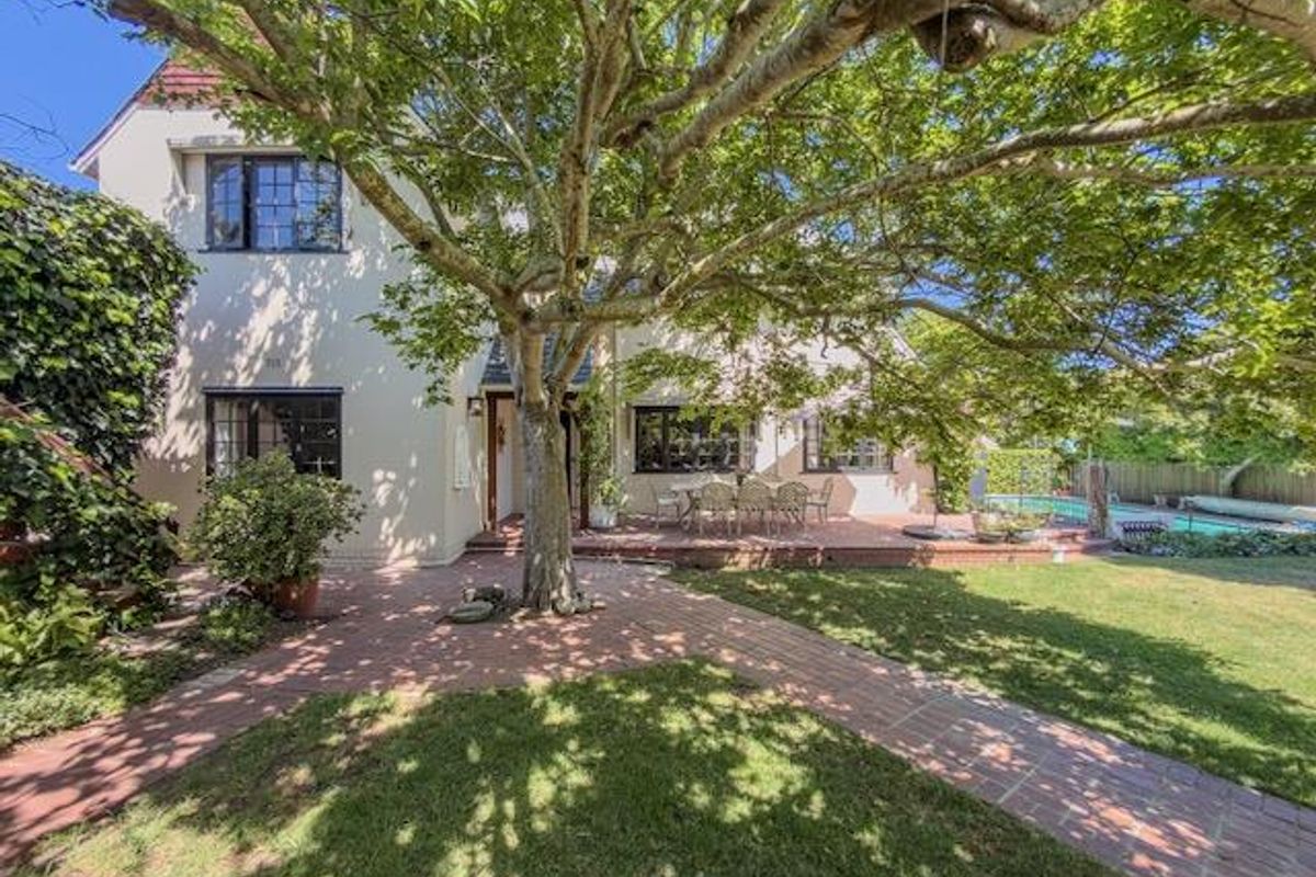 Rear view of the property featuring a brick paved patio, mature garden, and a swimming pool area.