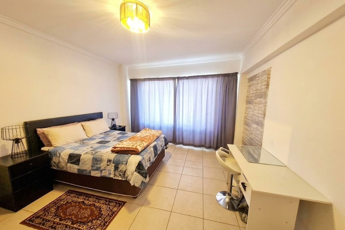 A spacious bedroom featuring tiled flooring, ceiling cornice detailing, and large windows with curtains, providing a functional and well-lit living space.