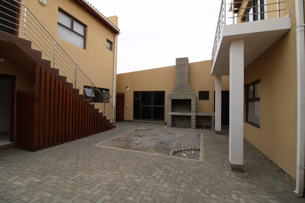 A paved rear courtyard featuring a built-in brick braai, external staircase with stainless steel railings, and covered patio area.