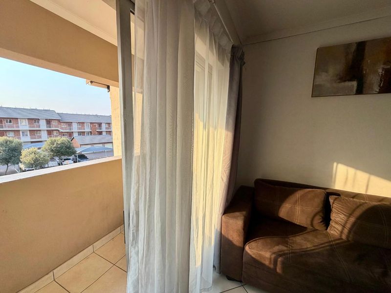 A balcony area featuring tiled flooring and a sliding glass door, providing an outdoor space with views of the surrounding apartment complex.