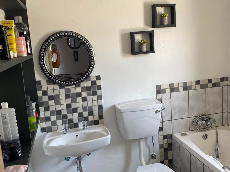 A functional bathroom featuring a wall-mounted basin, toilet, and bathtub with a tiled splashback and floor. The space shows signs of wear and dated finishes.