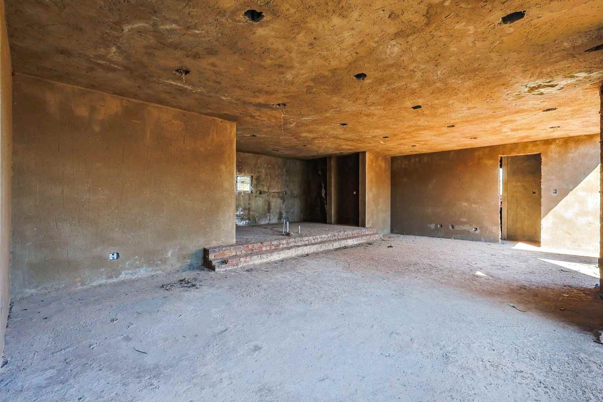 An unfinished interior space featuring raw plaster walls, exposed concrete ceilings, and a raised brick platform, offering a blank canvas for renovation.