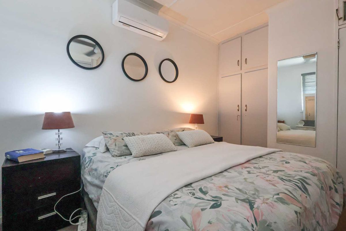 A well-maintained bedroom featuring built-in cupboards, a wall-mounted air conditioning unit, and neutral finishes.