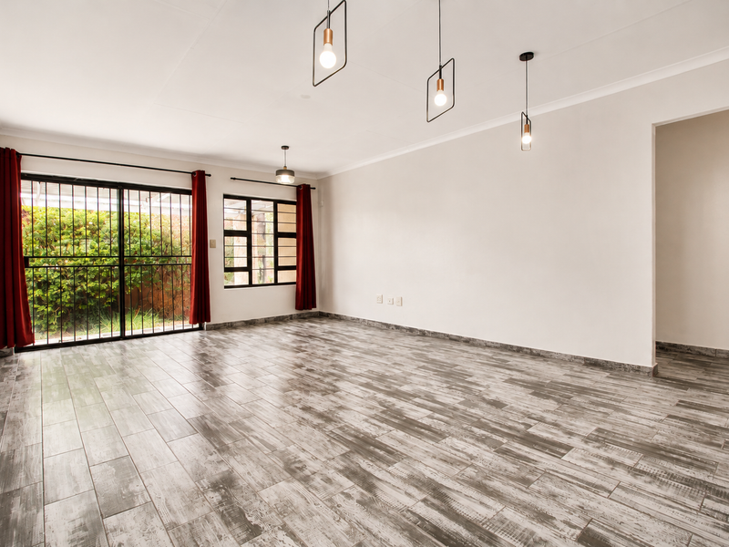 A bright and spacious living area featuring modern wood-look tile flooring, contemporary pendant lighting, and large sliding doors providing access to the garden.