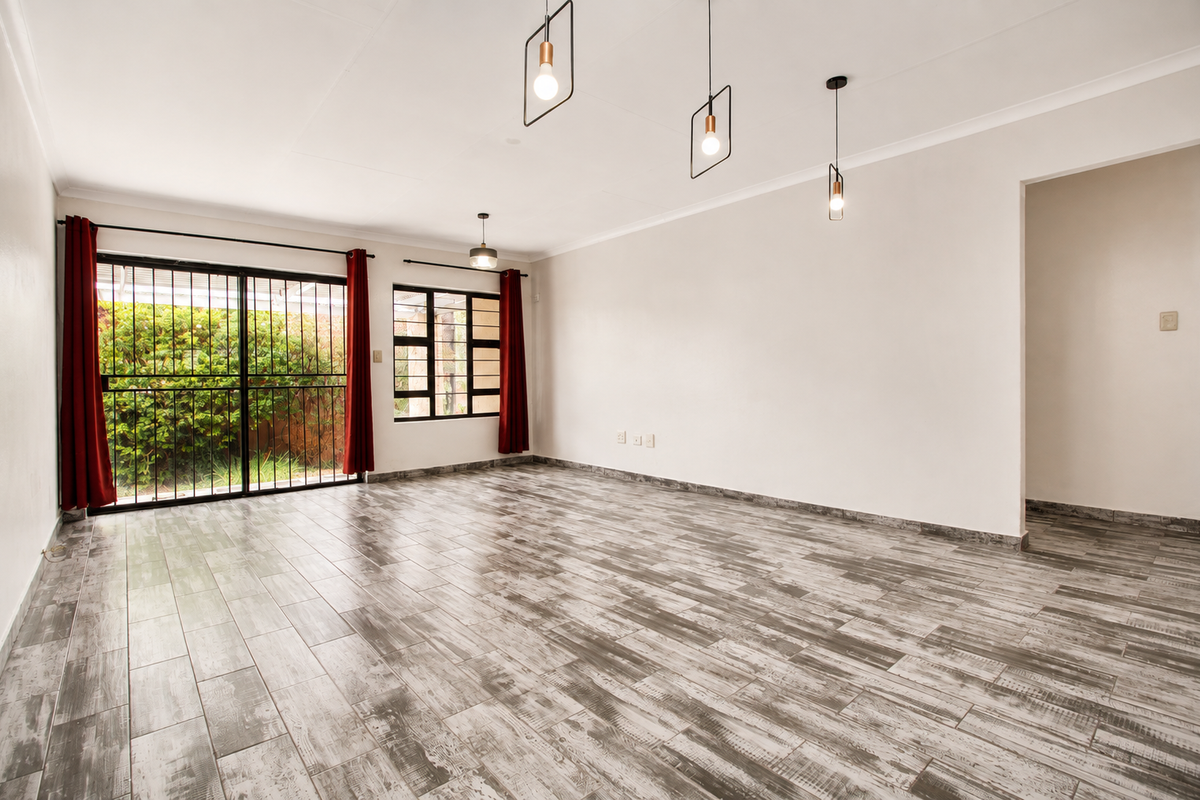 A bright and spacious living area featuring modern wood-look tile flooring, contemporary pendant lighting, and large sliding doors providing access to the garden.