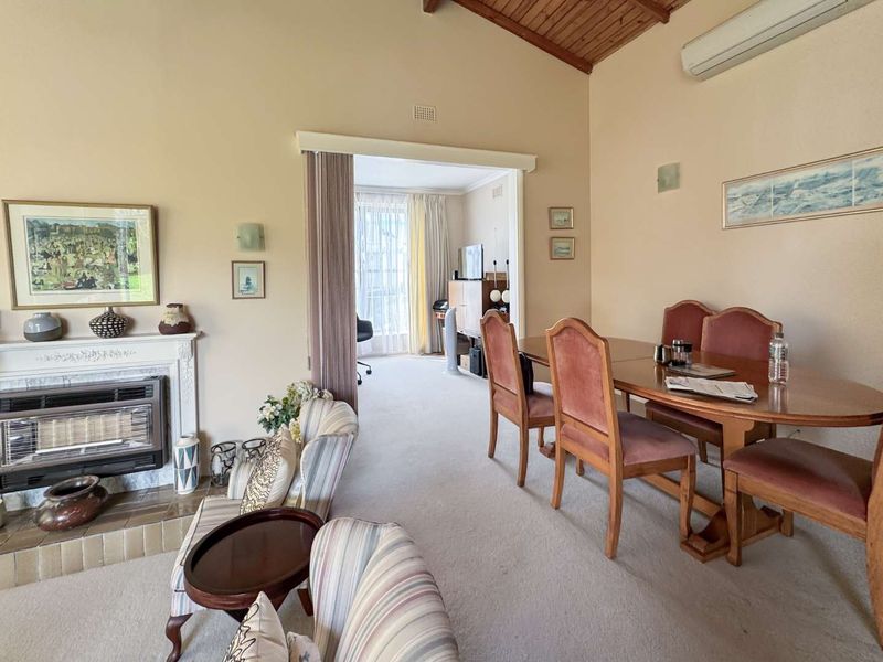 Spacious living and dining area featuring a fireplace, timber-lined vaulted ceiling, and split-system air conditioning, with an adjoining room visible through the doorway.
