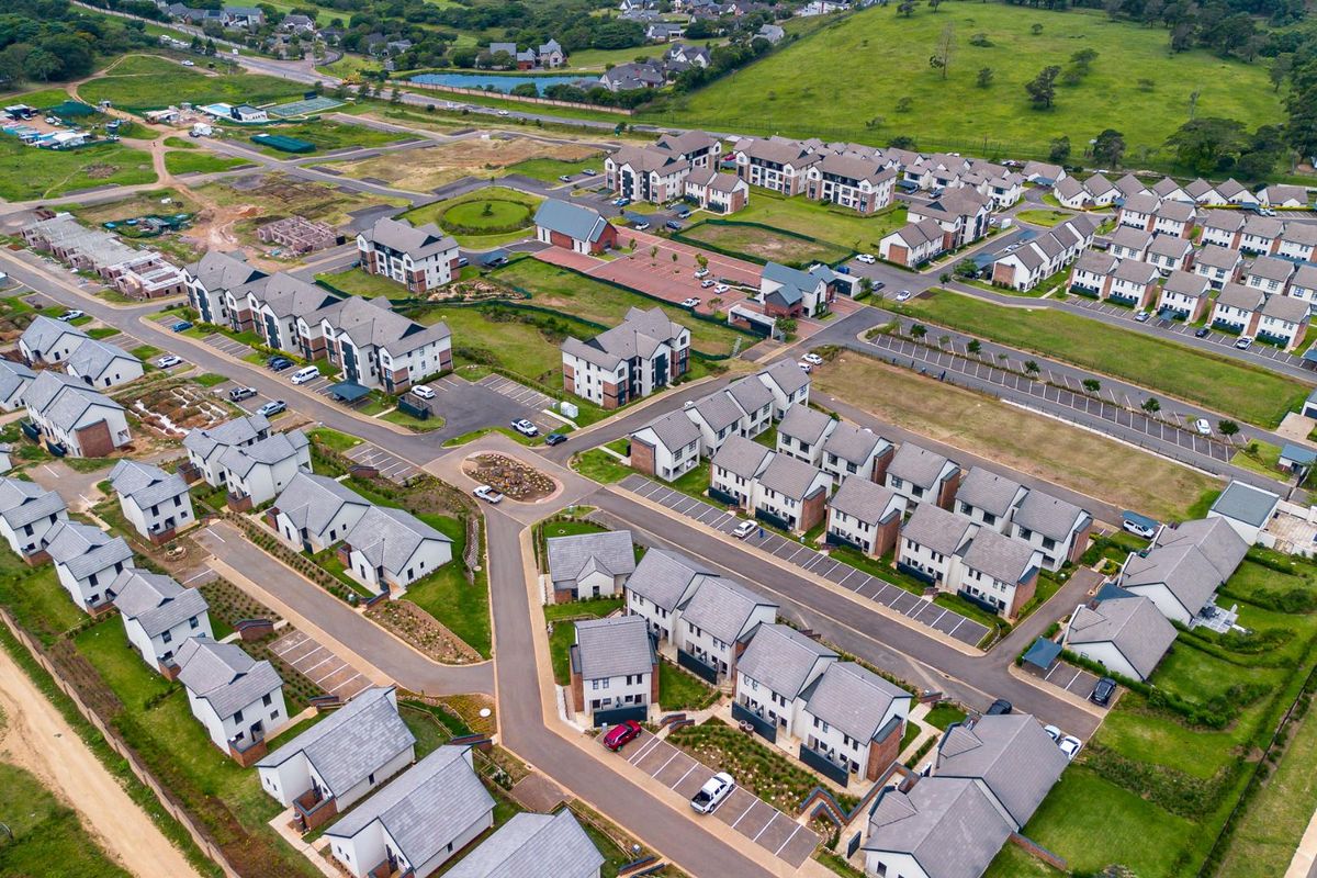 An aerial view of a modern residential apartment complex featuring multiple building blocks, paved parking areas, and surrounding landscaped grounds.