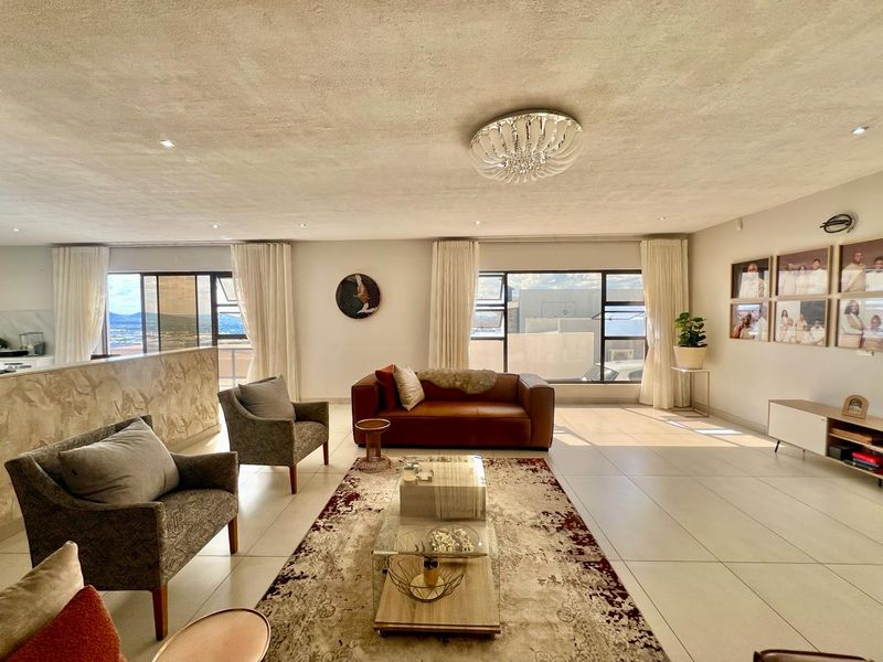 Spacious open-plan living area featuring large windows, neutral tiled flooring, and modern recessed lighting, creating a bright and airy atmosphere.