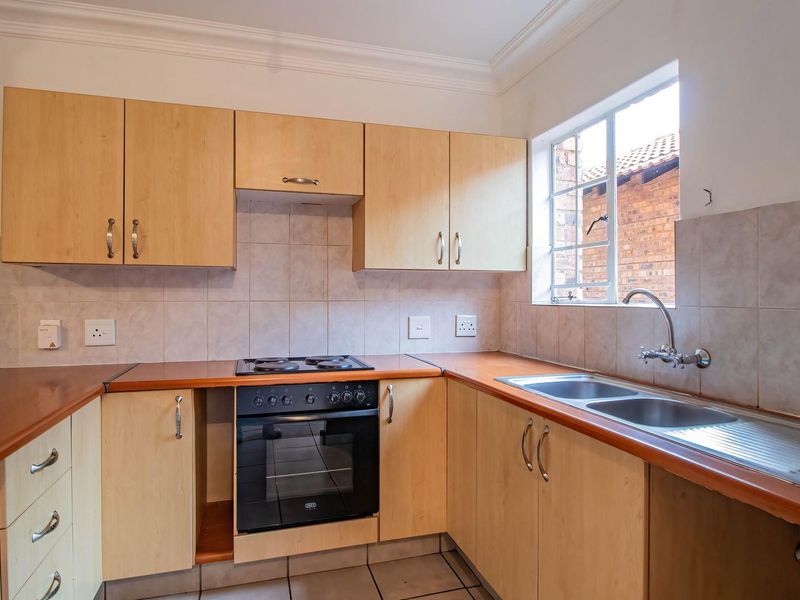 A functional kitchen featuring light wood cabinetry, laminate countertops, a built-in oven with electric hob, and a double bowl sink with tiled splashback.