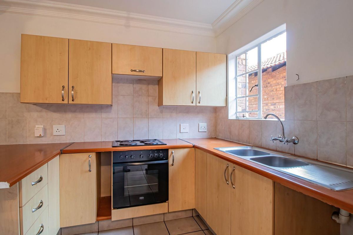 A functional kitchen featuring light wood cabinetry, laminate countertops, a built-in oven with electric hob, and a double bowl sink with tiled splashback.