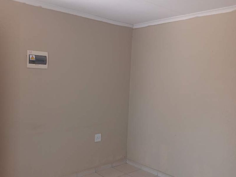 A simple, empty bedroom featuring neutral wall paint, tiled flooring, and a standard ceiling light fixture.