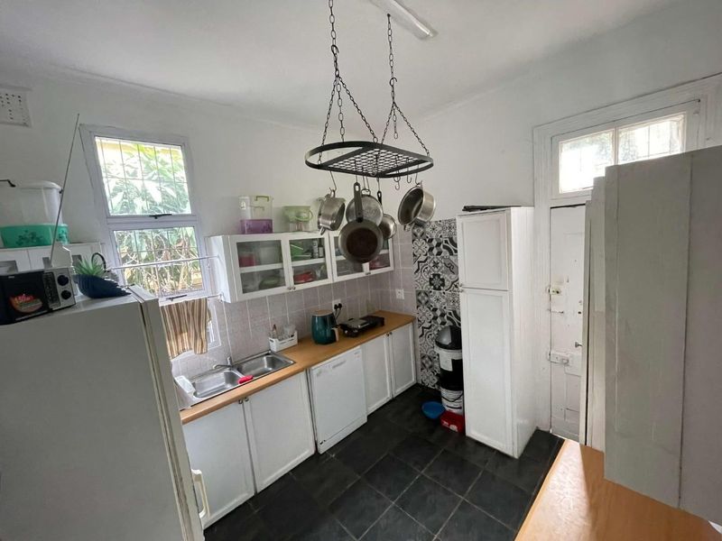 A functional kitchen featuring wooden countertops, double basin sink, built-in cabinetry, and a decorative tiled backsplash with dark floor tiles.