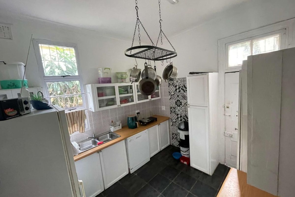A functional kitchen featuring wooden countertops, double basin sink, built-in cabinetry, and a decorative tiled backsplash with dark floor tiles.