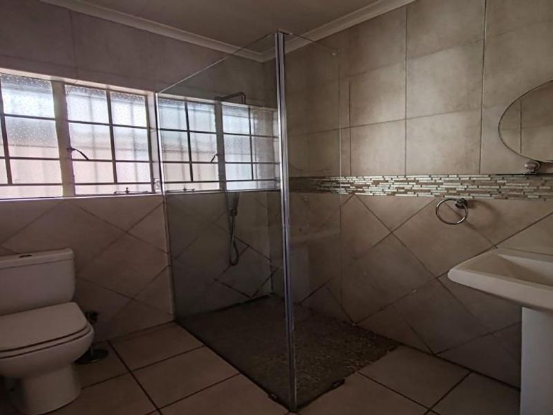 A functional bathroom featuring a walk-in shower with glass enclosure, pedestal basin, toilet, and neutral wall and floor tiling.