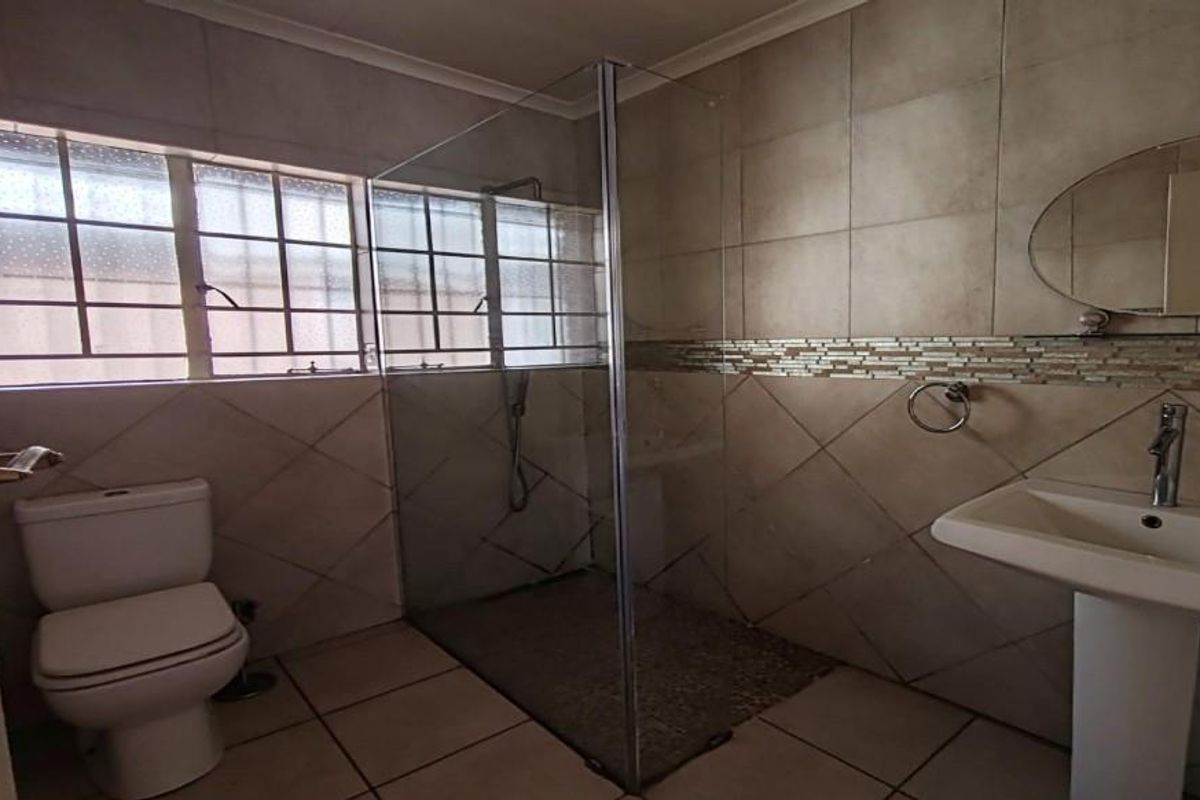 A functional bathroom featuring a walk-in shower with glass enclosure, pedestal basin, toilet, and neutral wall and floor tiling.