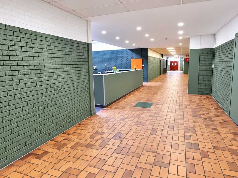 A spacious industrial hallway featuring durable tiled flooring, painted brick walls, and recessed ceiling lighting, providing a clean and functional circulation area.