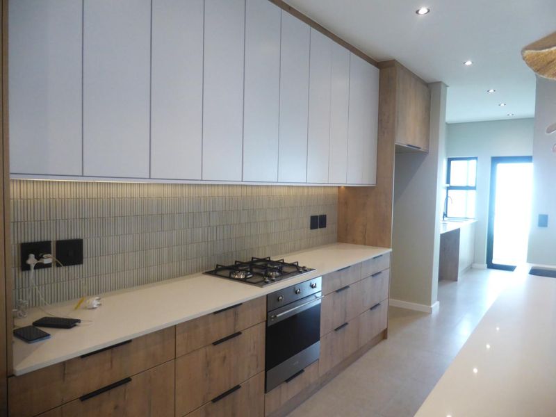 Modern kitchen featuring sleek white and wood-grain cabinetry, stone countertops, a gas hob, built-in oven, and stylish tiled backsplash with recessed lighting.
