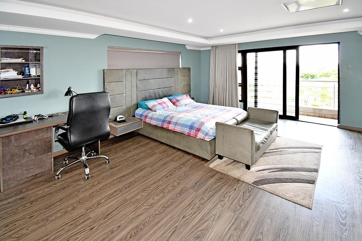 Spacious bedroom featuring wood-look laminate flooring, recessed ceiling lighting, a built-in desk area, and sliding glass doors leading to a private balcony.