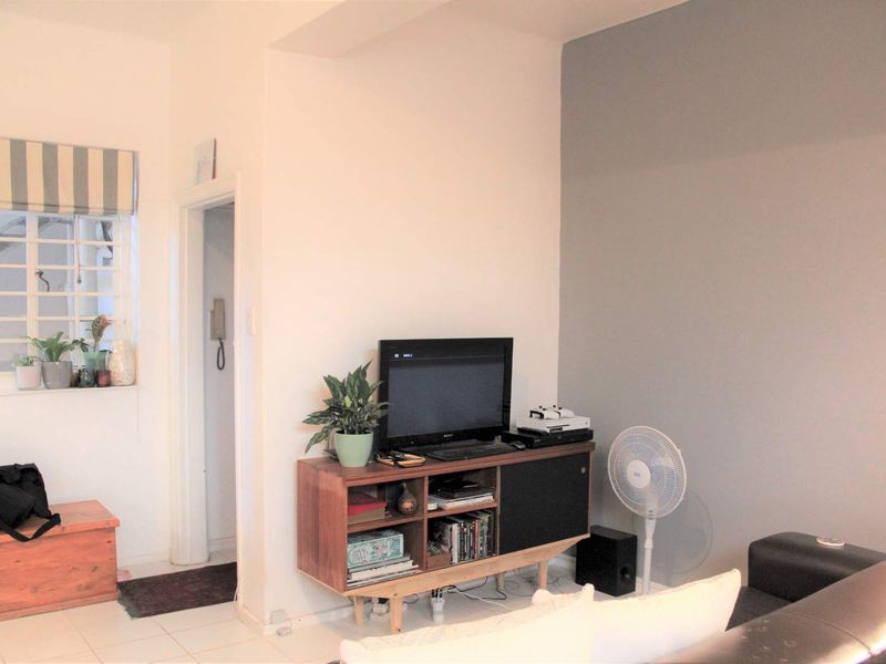 A living room area featuring tiled flooring, a window with security bars, and an intercom system installed near the doorway.