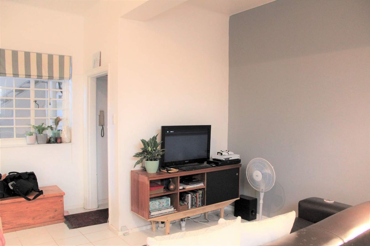 A living room area featuring tiled flooring, a window with security bars, and an intercom system installed near the doorway.