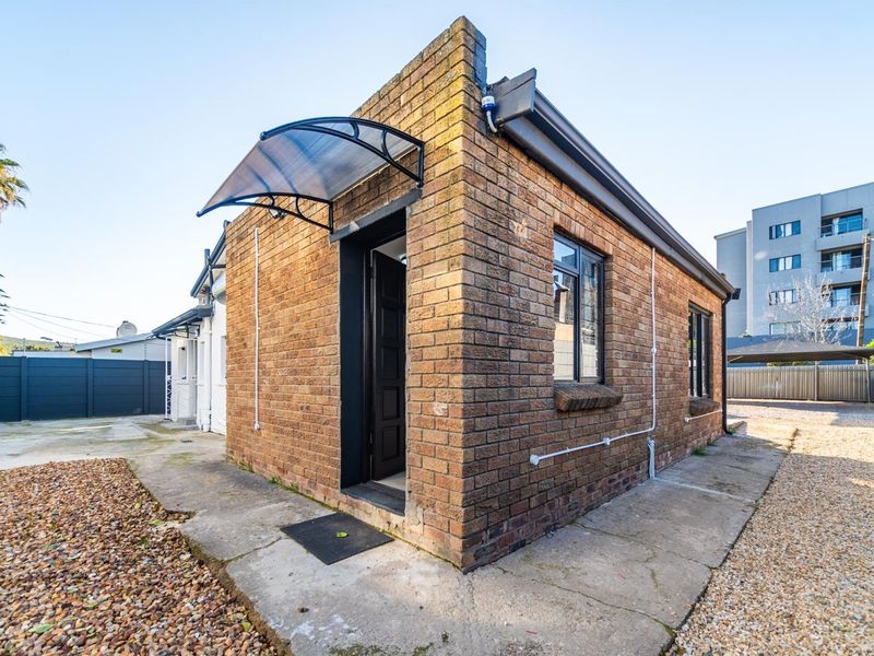 Exterior view of a face brick building featuring a polycarbonate door awning, aluminium window frames, and surrounding concrete pathways.