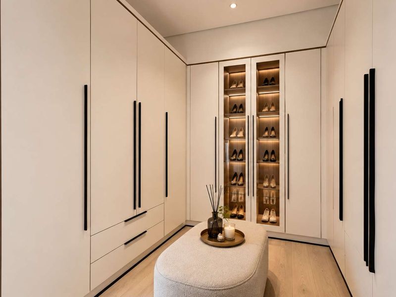 A modern, high-end walk-in closet featuring extensive floor-to-ceiling built-in cabinetry with integrated display shelving and sleek matte black hardware.