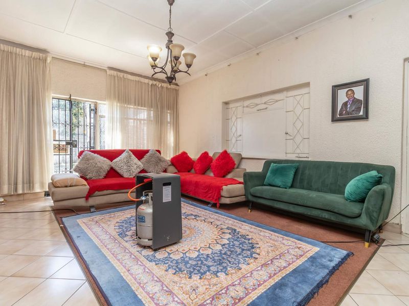 A living room featuring tiled flooring, a ceiling chandelier, and security bars on the windows, offering a functional space with potential for cosmetic updates.