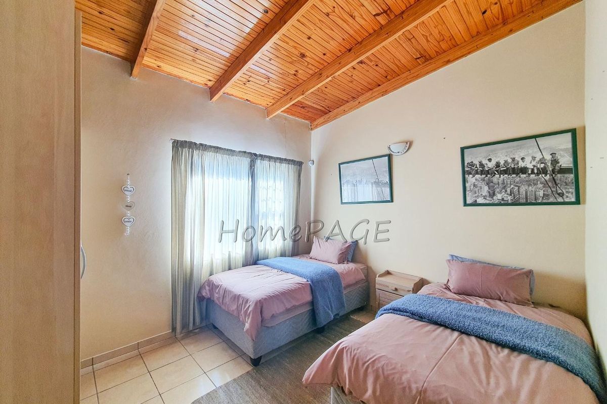 A bedroom featuring a high exposed timber beam ceiling, tiled flooring, and large windows allowing natural light.