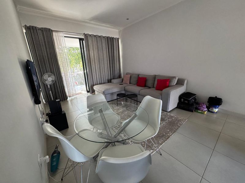 Open-plan living and dining area featuring large format floor tiles, neutral walls, and a sliding glass door providing access to an outdoor balcony.