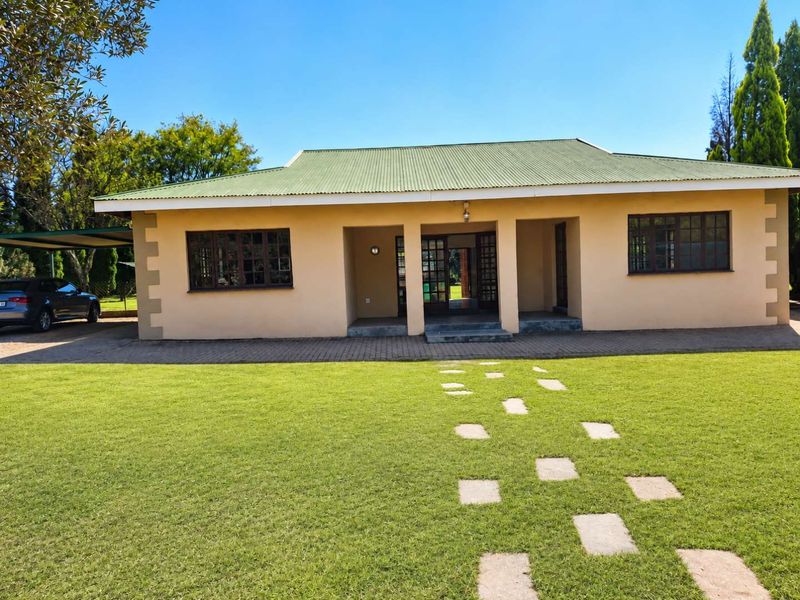 A single-story residential home featuring a green corrugated metal roof, paved driveway, carport, and a well-maintained front lawn with a stone pathway.