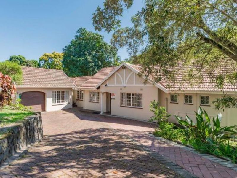 Front elevation of a well-maintained house featuring a tiled roof, brick driveway, and an integrated garage, surrounded by established garden landscaping.