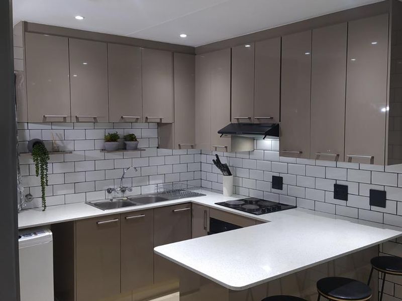 Modern kitchen featuring glossy cabinetry, subway tile backsplash, quartz countertops, and integrated appliances, including a gas hob and built-in oven.