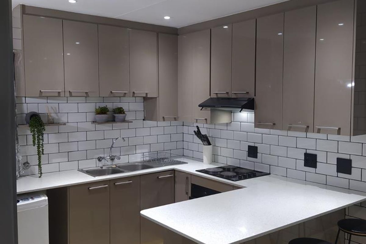 Modern kitchen featuring glossy cabinetry, subway tile backsplash, quartz countertops, and integrated appliances, including a gas hob and built-in oven.