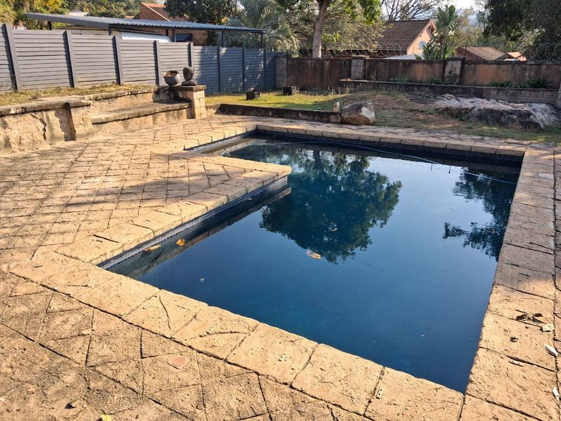 Outdoor pool area featuring a swimming pool with stone coping, a built-in stone bench, and perimeter fencing.