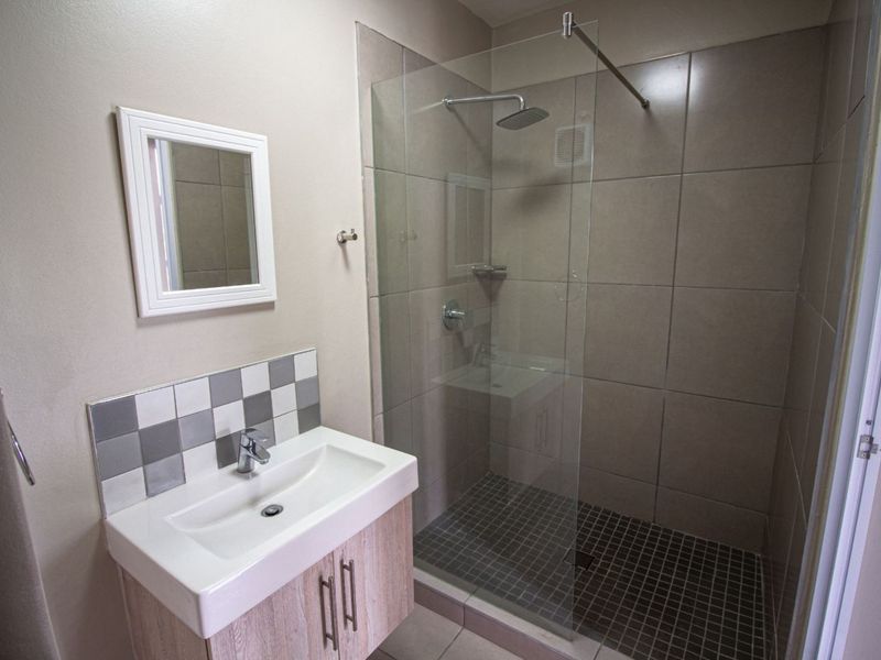 A modern bathroom featuring a vanity cabinet with a ceramic basin, a glass-enclosed shower with mosaic floor tiles, and neutral wall tiling.