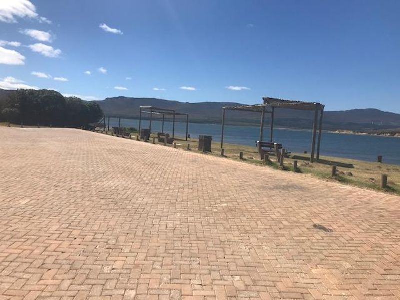 A scenic view of a paved parking area overlooking a large body of water with timber pergolas and mountain vistas in the background.
