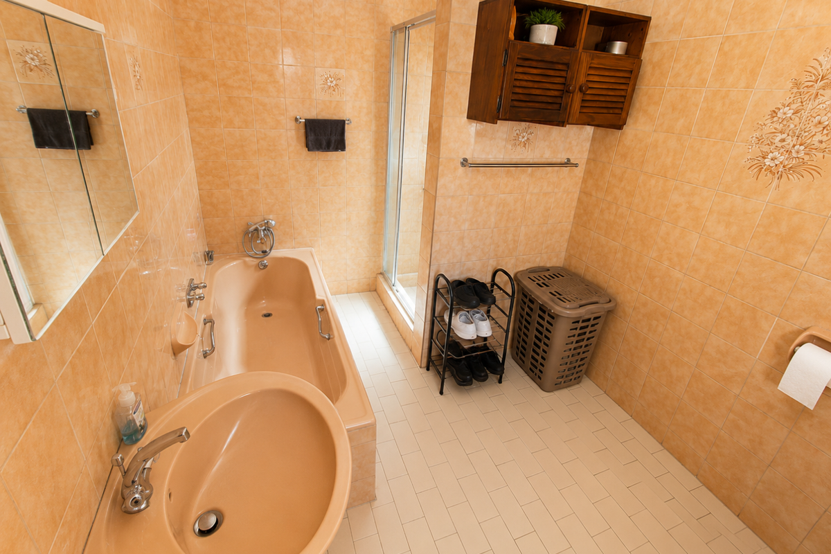 A functional bathroom featuring a built-in bathtub, separate shower enclosure, and vanity basin, finished with dated wall tiles.