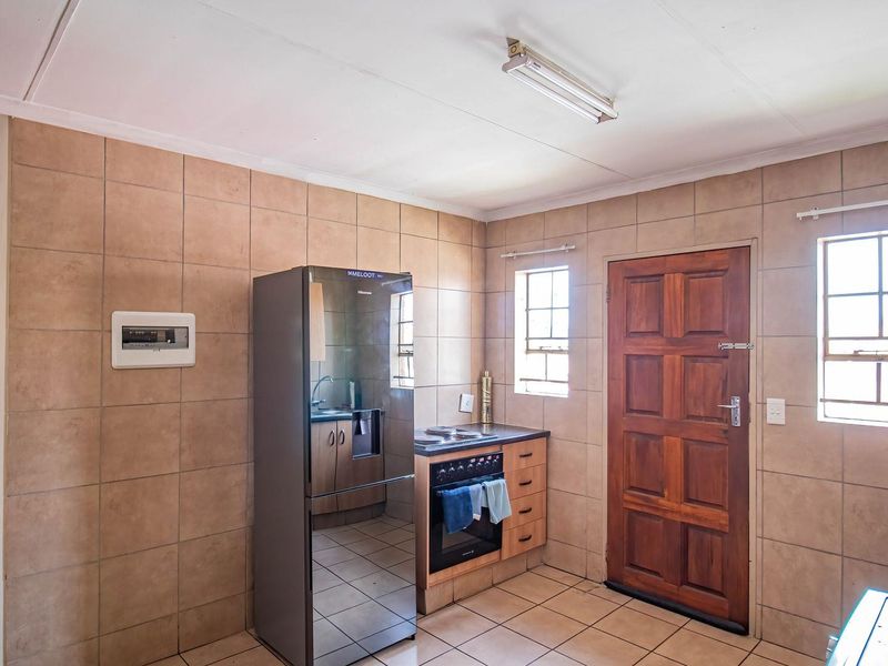 A functional kitchen featuring tiled walls and flooring, a built-in oven with hob, and direct exterior access via a timber door.