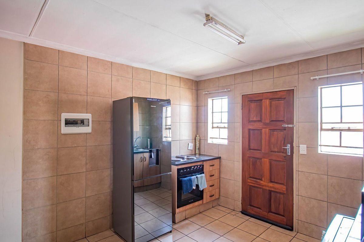 A functional kitchen featuring tiled walls and flooring, a built-in oven with hob, and direct exterior access via a timber door.