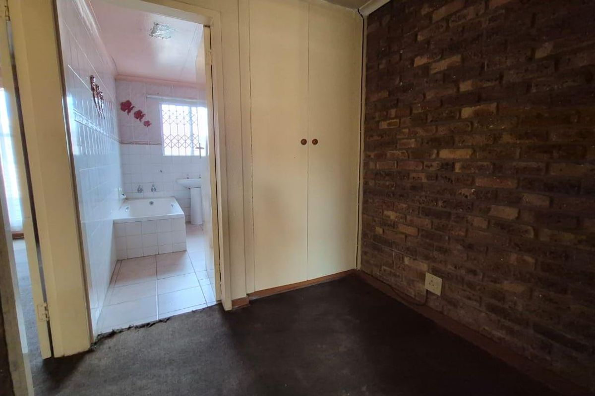 Bedroom featuring exposed brickwork and built-in cupboards, with an adjoining bathroom visible through the doorway.