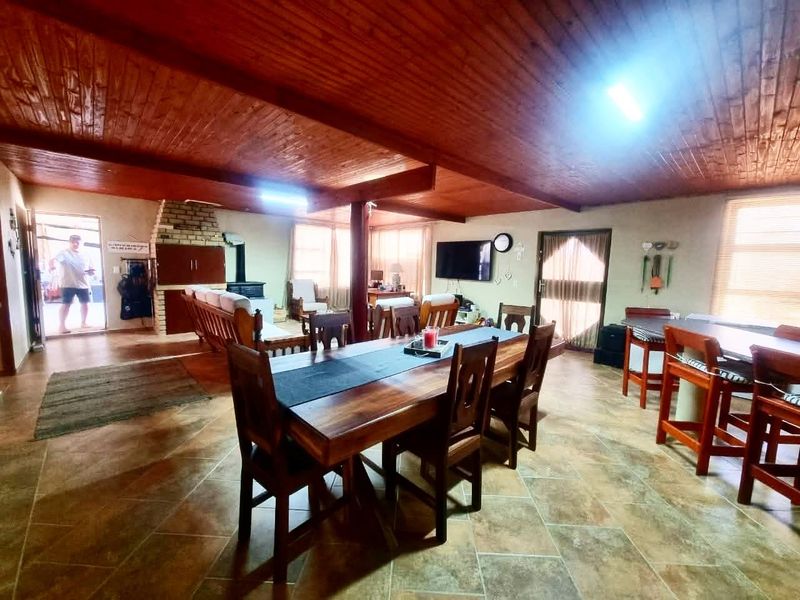 Spacious open-plan living and dining area featuring a rustic timber ceiling, tiled floors, and a traditional brick fireplace.