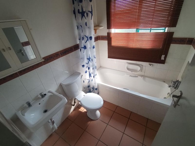 A functional bathroom featuring a bathtub, wall-mounted basin, and toilet, finished with tiled walls and flooring, requiring cosmetic updates to modernize the space.