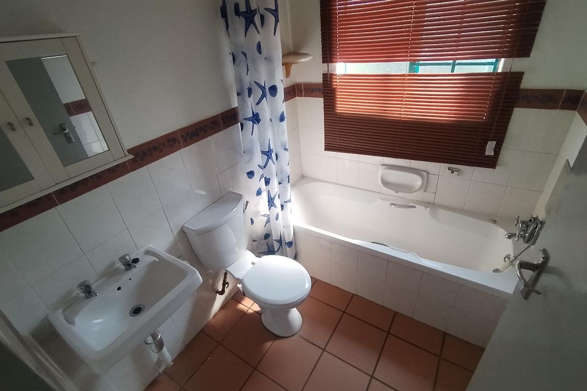 A functional bathroom featuring a bathtub, wall-mounted basin, and toilet, finished with tiled walls and flooring, requiring cosmetic updates to modernize the space.