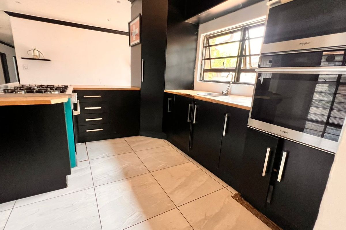Modern kitchen featuring black cabinetry, light wood countertops, built-in oven, gas hob, and tiled flooring.