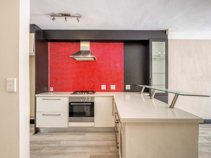 Modern kitchen featuring a striking red mosaic backsplash, built-in oven, gas hob, extractor fan, and a sleek breakfast bar with quartz countertops.