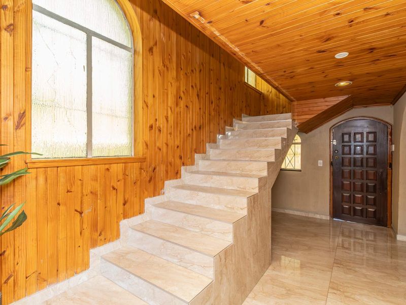 Spacious entrance hall featuring a tiled staircase, timber wall paneling, and a warm timber ceiling with recessed lighting.