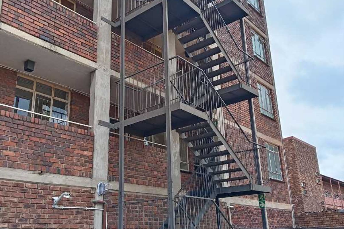 Rear elevation of a multi-story apartment building featuring a prominent external steel fire escape staircase and face brick exterior finish.
