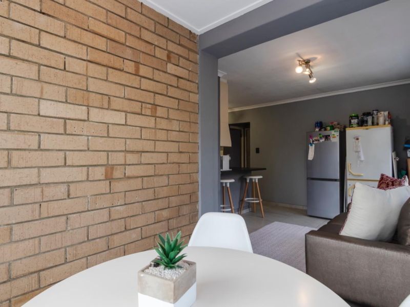 Open plan living area featuring an exposed brick wall, tiled flooring, and a breakfast bar connecting to the kitchen space.