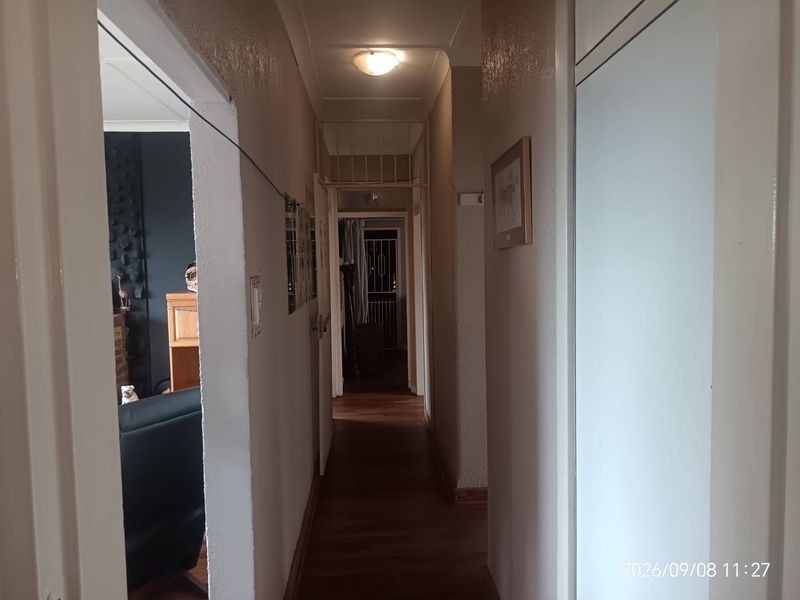 A functional residential hallway featuring laminate flooring, built-in storage cupboards, and overhead lighting, providing access to adjacent living areas.